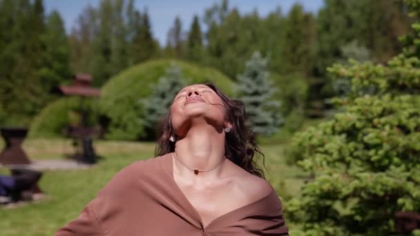 一个女舞蹈演员的画像，白天在一个绿色的公园散步，把胳膊伸向两边，望着阳光下的天空，她在度假时很高兴 — 图库视频影像
