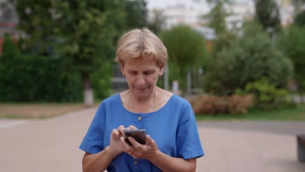 Una mujer, una pensionista solitaria, camina por las calles durante el día y usa el teléfono para comunicarse con sus familiares. — Vídeos de Stock