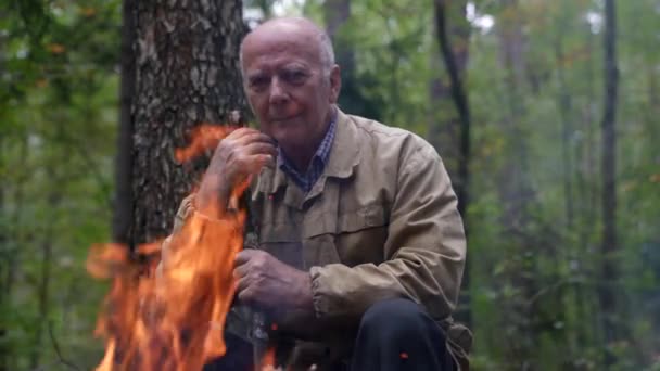 Портрет старого в лісі, який зігрівається біля багаття, дивлячись і пам'ятаючи життя — стокове відео