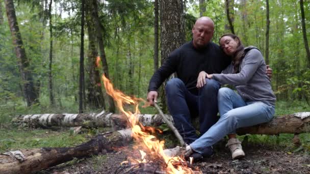 Um cara abraça um amigo, sentado junto a uma fogueira aconchegante em um piquenique em uma maravilhosa floresta de outono colorido. Um casal adulto em férias — Vídeo de Stock