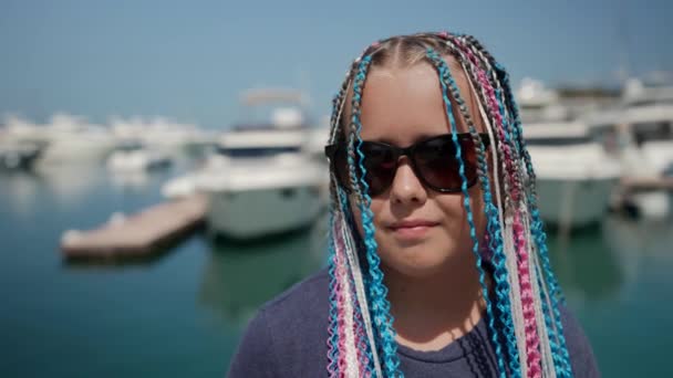 Porträt einer Hippie-Teenagerin mit Afro-Zöpfen im Haar steht am Nachmittag bei sonnigem Wetter vor dem Hintergrund der Hafenstadt — Stockvideo
