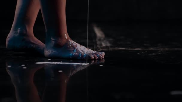Крупный план в темноте женской ноги, идущей по черному полу и проливающей художественную импровизацию — стоковое видео