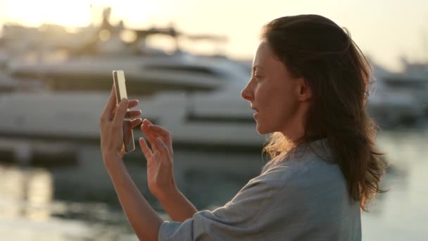 一个成年的自然女人在黄昏的时候写下了一条信息，她站在海港边 — 图库视频影像