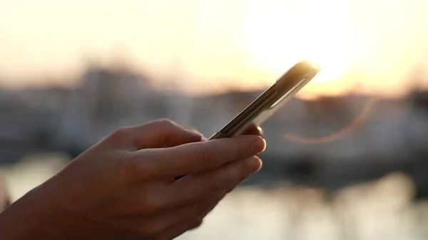 Vue latérale de la main d'une femme utilisant un smartphone sur la plage au coucher du soleil ou au lever du soleil. Gros plan sur les mains des jeunes femmes Photo De Stock