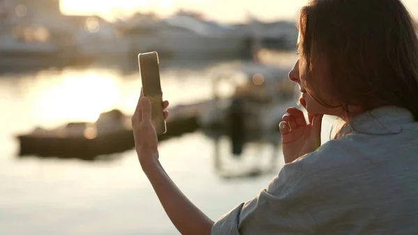 Portrait d'une femme avec les rayons du soleil couchant sur un appel vidéo avec un smartphone. Le concept moderne de l'utilisateur de la technologie sans fil. Images De Stock Libres De Droits
