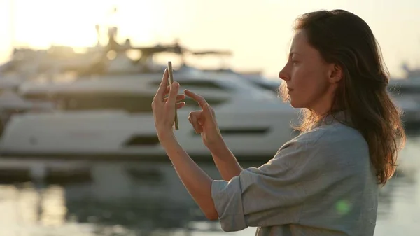 Portrét turistické ženy s telefonem psaní zpráv na dotykovém displeji při západu slunce u pobřeží Stock Obrázky