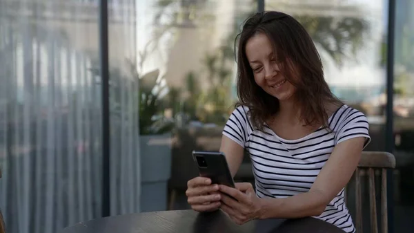 Dospělá žena píše, posílá SMS do smartphonu, během dne sedí v kavárně Stock Obrázky