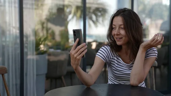 Dospělá žena sedí na verandě restaurace a mluví na video spojení s telefonem Royalty Free Stock Fotografie