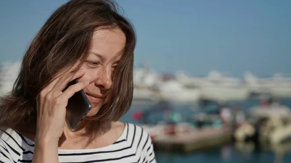 Une jolie femme d'âge moyen parle au téléphone dans la rue par un matin ensoleillé Images De Stock Libres De Droits