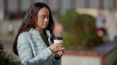 Düşünceli orta yaşlı bir kadının portresi. Güneşli bir sonbahar gününde, elinde bir fincan sıcak kahveyle sokakta oturuyor ve düşünüyor.