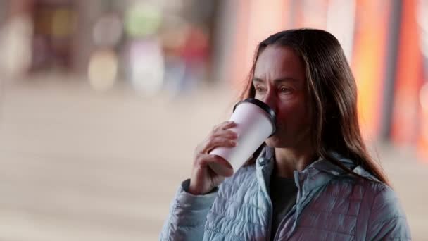 Porträt einer erwachsenen Frau mit großen Falten unter den Augen, die auf der Straße Kaffee aus einem Pappbecher trinkt — Stockvideo