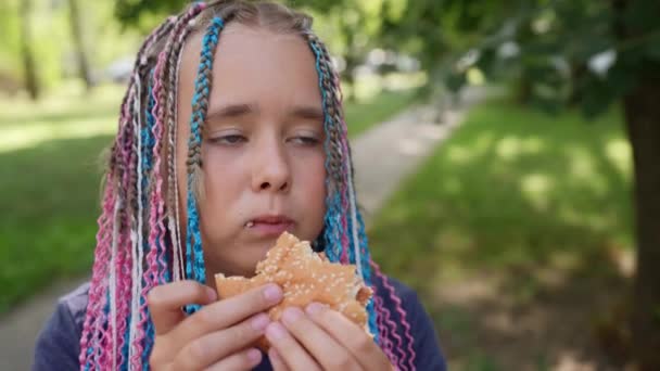 Портрет модной девочки-подростка, которая ест на улице бургер с курицей — стоковое видео