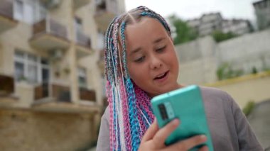 Afro örgülü neşeli bir kız çocuğunun portresi sokakta telefonla konuşuluyor.