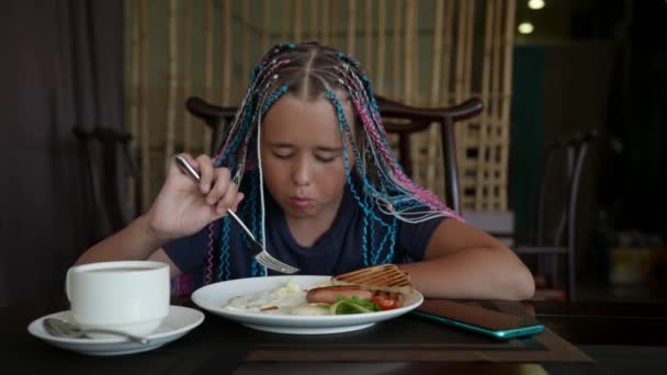 Una ragazza adolescente elegante con le trecce afro tra i capelli sta facendo colazione in un ristorante al mattino — Video Stock