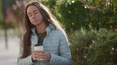 Yetişkin, güzel bir kadın bankta beyaz bir fincanda kahve ile oturuyor.