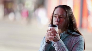 Hazır kahve içen yetişkin bir kadının portresi. Bir şehir caddesinde elinde bir bardak sıcak içecekle duran doğal yetişkin bir kız.