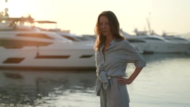 Привлекательная успешная женщина позирует вечером на фоне дорогой яхты в море лучи заходящего солнца — стоковое видео