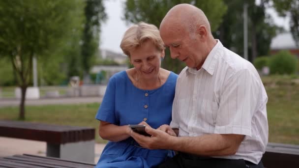 Un couple âgé d'un homme caucasien et sa femme sont assis dans le jardin près de la maison et avoir un appel vidéo à l'aide d'un téléphone mobile — Video