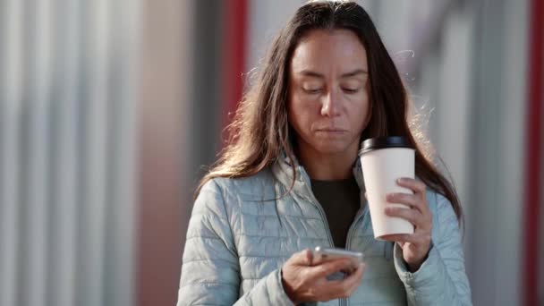 一个拿着手机和纸杯的女人的画像。一个成年女人用智能手机写短信，喝外卖咖啡 — 图库视频影像