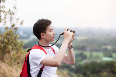 Sırt çantalı genç turist kayalık dağda oturuyor ve kameradan fotoğraf çekiyor. Seyahat kavramı.