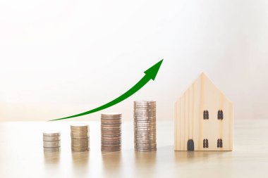 Mini ahşap ev ve üzerinde yeşil ok olan bozuk paralar. Ev almak için para yatırımı. Yatırım sektörü kavramı.