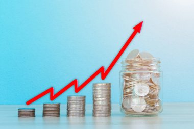Kırmızı oklar bozuk paraların üzerinde, cam şişede bozuk paralar var. İş büyümesi ve tasarruf veya yatırım kavramı.