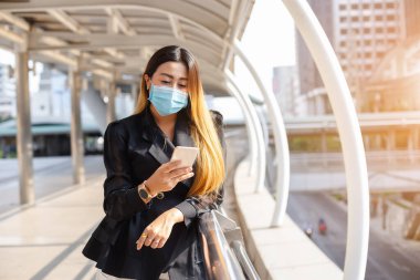 Toz ve enfeksiyonu önlemek için tıbbi maske takan Asyalı kadın, şehir merkezinde akıllı telefon ya da cep telefonu kullanıyor..