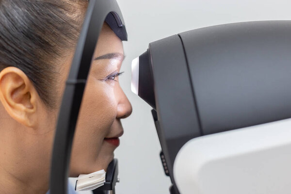 Close up face of middle aged asian woman examining eyesight modern machine equipment in clinic.