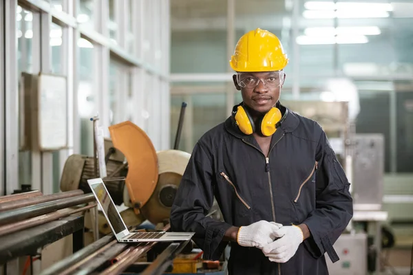 Portrait of black male african american workers wear sound proof headphones and yellow helmet standing an iron cutting machine in factory Industrial.