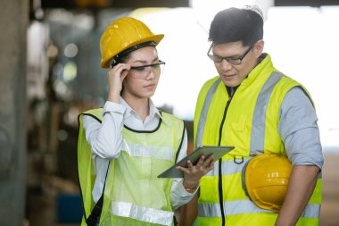 Fabrikada çalışan Asyalı erkek ve kadın mühendis dijital tablet kullanarak projeden bahsediyorlar. Ağır sanayi fabrikası konsepti.