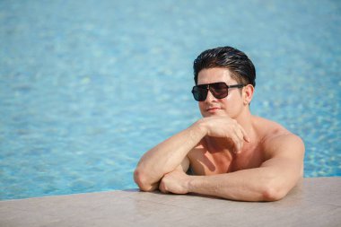 Yakışıklı adam güneş gözlüğü takıyor havuz başında dinleniyor, tatilde hayat tarzı seyahat ediyor. Rahatlama kavramı.