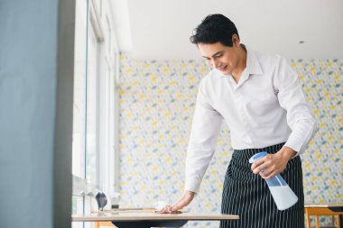 Restoranda sterilize etmek için Asyalı genç adam beyaz gömlek temizleme masası ve sprey alkol. işyerinde çalışan temizliği.