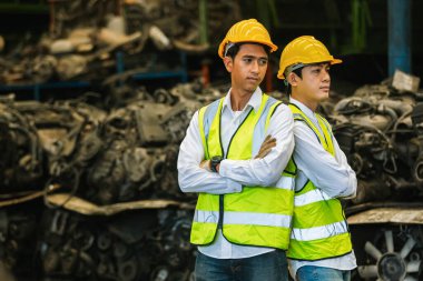 İki mühendisin portresi, işçi üniforması ve kask kolu depoda kesişiyor. İşyeri fabrikası ağır makine sanayisi.