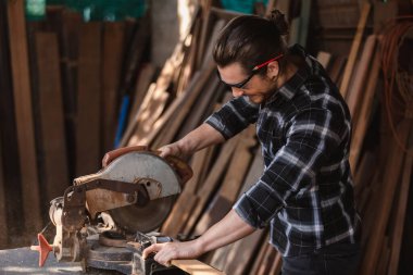 Genç marangoz elektrikli testereyle odun kesiyor. Ahşap fabrikasında zanaatçılık mesleği.