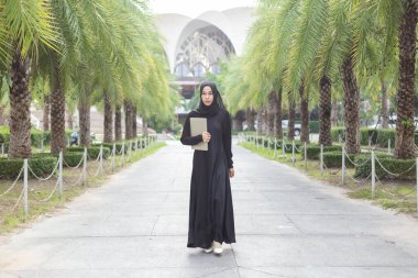 Siyah tesettürlü Müslüman kadının portresi dizüstü bilgisayarın arka planını taşıyor..