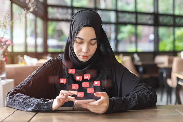 アジアの若いイスラム教徒の女性は スマートフォンの通知ソーシャルメディアのアイコン インターネットデジタルマーケティングの概念を使用して黒いヒジャーブを身に着けている — ストック写真