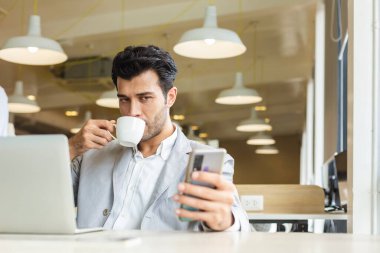 Yakışıklı iş adamı rahatlamak için akıllı telefon kullanıyor. İşyerinde oturan dizüstü bilgisayarlı bir erkek..