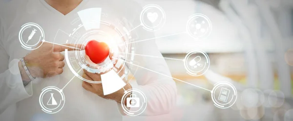 Man holding red heart in hand attaches chest and finger point with medical icon network connection. Health care concept. Crop image banner size.