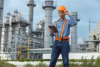 Güvenlik kaskı takan Asyalı endüstriyel mühendis elektrik santralini incelerken dijital tablet tutuyor, akıllı endüstriyi, dijital mühendisliği ve mesleki güvenliği temsil ediyor..