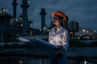 Elektrik santralinde gece vardiyası sırasında güvenlik kaskı takan kadın sanayi mühendisi, mühendislik ve inşaat sektöründe liderlik, planlama ve çeşitliliği sembolize ediyor..