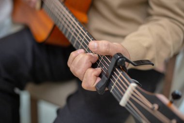 Yaşlı bir adamın Capo kullanarak akustik gitar çaldığı, ayrıntılı parmak yerleştirme ve akor tekniğini gösteren yakın plan fotoğrafı. Müzik terapisi, rahatlama ve son sınıf hobileri kavramı.