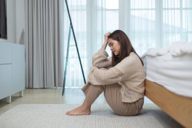 Yatağın yanında oturan Asyalı kadınlar duygusal çöküntü, depresyon konsepti, ruhsal sağlık sorunları, tükenmişlik, yalnızlık ve duygusal yorgunluk ile başını tutuyorlar..