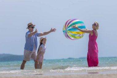 Mutlu bir aile yaz tatilinde sahilde renkli bir plaj topuyla oynuyor. Aile bağı, seyahat, plaj eğlencesi, açık hava yaşam tarzı ve tatil mutluluğu kavramı.