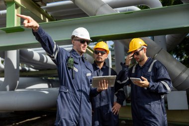 İnşaat alanında tablet ve telsiz kullanarak güvenlik kaskı takan endüstri mühendisleri ekibi takım çalışması, mühendislik planlaması, rafineri denetimi ve saha denetimini temsil ediyor..