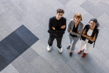 Kendine güvenen farklı iş adamları, kollarını kavuşturup yukarıdan bakıyorlar. Birliğin, liderliğin, takım çalışmasının ve modern bir çevreye güvenin temsilcileri..