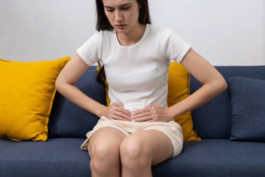 Kanepede otururken karın ağrısı çeken kadınlar, sindirim sorunları, gıda zehirlenmesi, regl sancıları veya sağlık ve tıbbi içerikteki karın ağrıları.