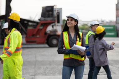 Konteynır deposundaki operasyonları incelerken güvenlik yeleği ve miğfer taşıyan kadın lojistik denetçisi, liderlik, planlama ve profesyonel yönetimi temsil ediyor..