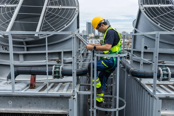 Güvenlik üniformalı endüstriyel teknisyen çatıdaki havalandırma sistemine erişmek için merdivene tırmanıyor. Mühendislik güvenliği, altyapı ve mekanik işlemleri temsil ediyor..