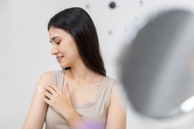 Asyalı kadınlar omuzlarına gülümseyerek nemlendirici krem sürüyor, cilt bakımını, güzellik düzenini ve evde kişisel sağlığını teşvik ediyor, doğal güzellik ve günlük kişisel bakım alışkanlıklarını vurguluyor.