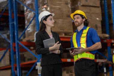 Depo yöneticisi ve işçi depolama tesisinde dijital tabletler kullanarak lojistik görevleri tartışıyor. Takım çalışması, akıllı tedarik zinciri yönetimi ve profesyonel depo işbirliği kavramı.